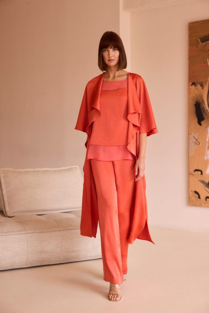 Abito da cerimonia Carla Ruiz con pantalone largo arancione, maglia a trama larga e blusa lunga sovrapposta.
